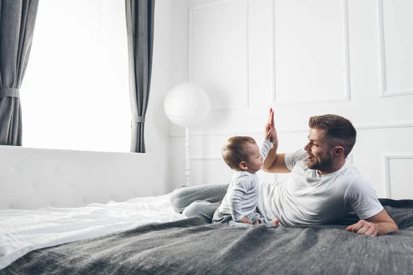 Lycklig far med sin son som spelar hemma på sängen — Stockfoto