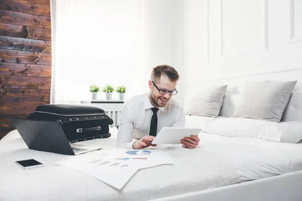 Empresario en la cama trabajando con una tableta y un portátil desde su habitación de hotel — Foto de Stock