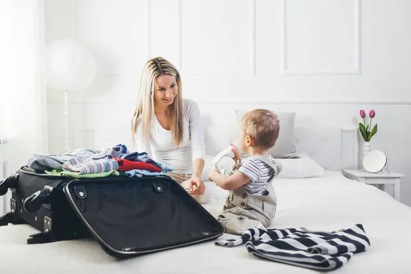 Reisen mit Kindern. glückliche Mutter mit ihrem Kind, das Kleidung für den Urlaub einpackt — Stockfoto