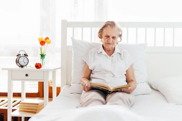 Mujer mayor sentada cómodamente en la cama leyendo su libro favorito —  Fotos de Stock