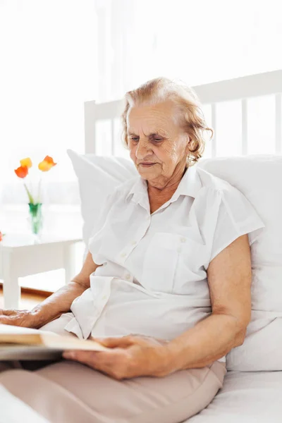 Mujer mayor sentada cómodamente en la cama leyendo su libro favorito —  Fotos de Stock