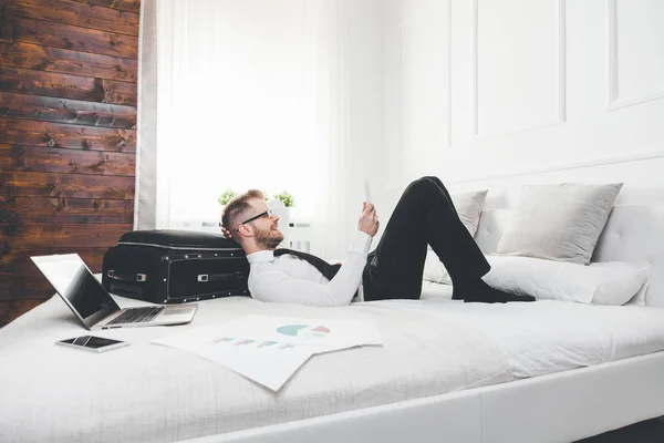 Empresario en la cama trabajando con una tableta y un portátil desde su habitación de hotel — Foto de Stock