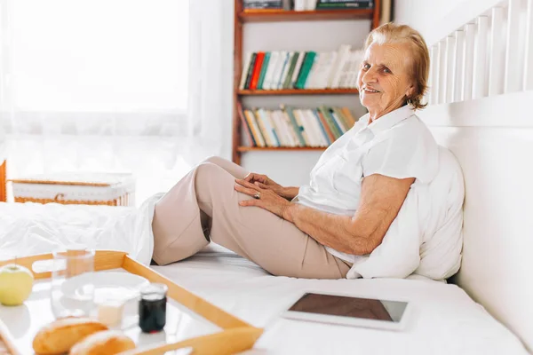 Femme âgée prenant son petit déjeuner au lit en utilisant sa tablette — Photo