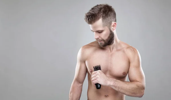 Handsome bearded man with a trimmer shaving off body hair — Stock Photo, Image