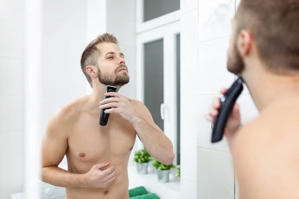 Hombre barbudo guapo recortando su barba con un trimmer — Foto de Stock