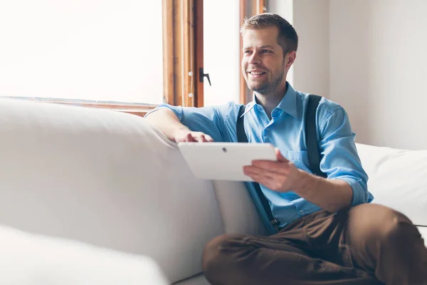 Pohledný muž sedí na pohovce v digitálním tabletu — Stock fotografie