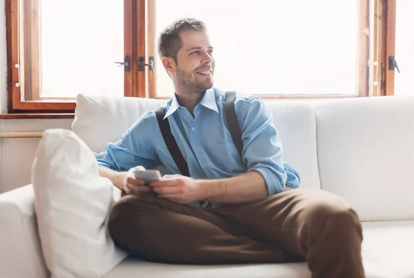 Schöner Mann sitzt auf Sofa und SMS — Stockfoto