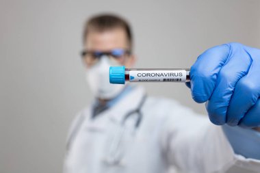 Doktor solunum maskesi takıyor ve Coronavirus Covid-19 kan örneğini tutuyor. 
