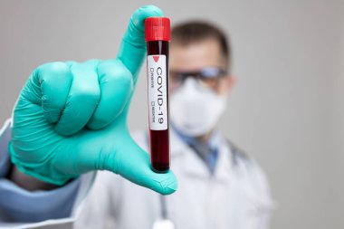 Doktor solunum maskesi takıyor ve Coronavirus Covid-19 kan örneğini tutuyor. 
