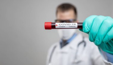 Doktor solunum maskesi takıyor ve Coronavirus Covid-19 kan örneğini tutuyor. 