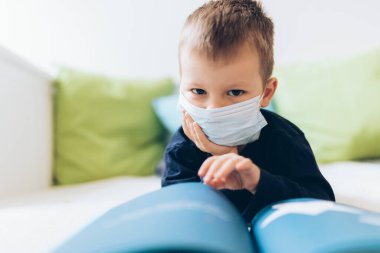 Coronavirus Covid-19 'a karşı önlem olarak solunum maskesi takan mutsuz bir çocuk.