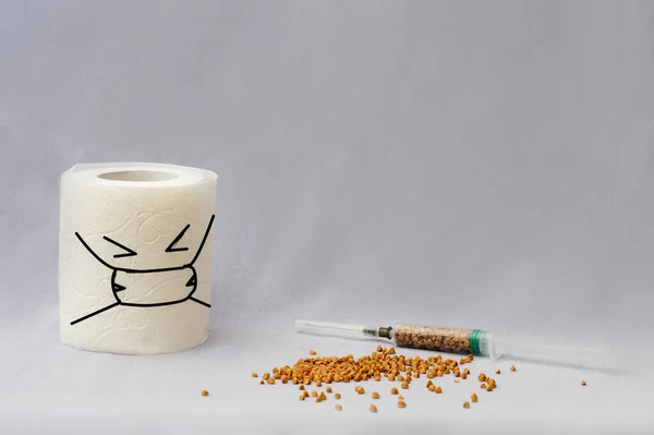 Yüzü çizilmiş bir rulo tuvalet kağıdı ve arka planında karabuğday olan bir şırınga. Kendini izole etme, karantina, koronovirüsün arka planında panik. Sağlığınıza dikkat edin. Salgın.