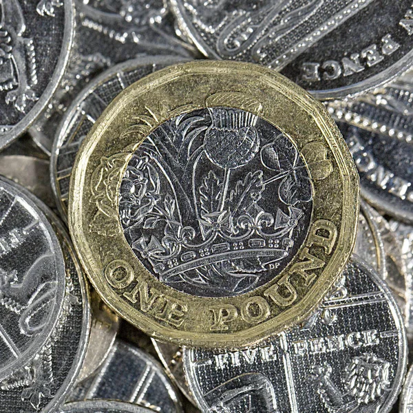 Close up of a British One Pound coin on a selection of five pence pieces in a square format