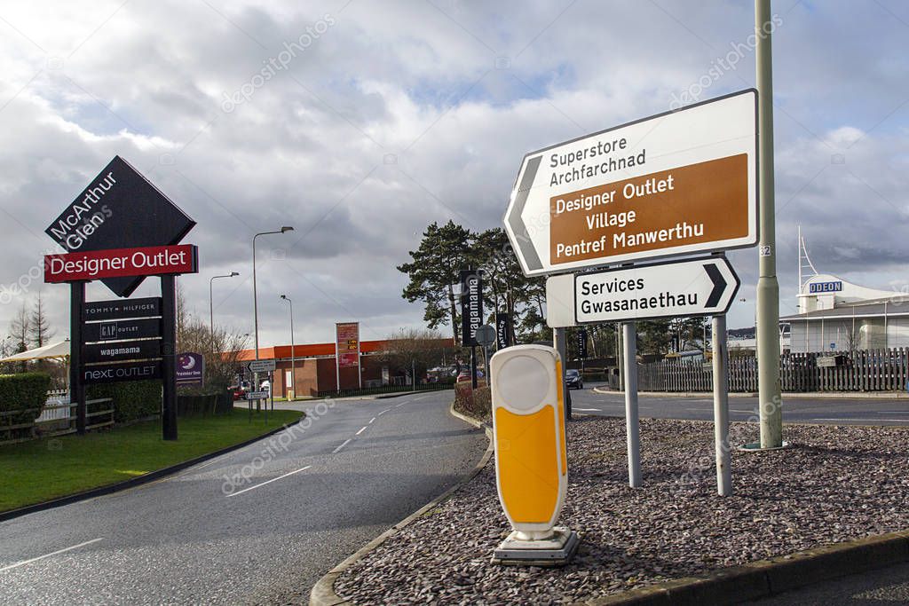 Bridgened, UK: January 14, 2017: Road sign indicating the way to a Designer Outlet Village. McArthurGlen Group is a public company, a developer and manager of designer outlet malls. An Odeon cinema and Sainsbury shop can be seen in the background.