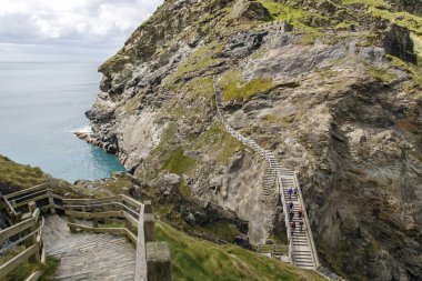 Cornwall, İngiltere: 14 Nisan 2016: Tintagel adaya ahşap köprüyü geçtikten turistler. Tintagel ayrıca İngiltere diğer siteler için sorumlu İngiliz Heritage tarafından yapılmaktadır.
