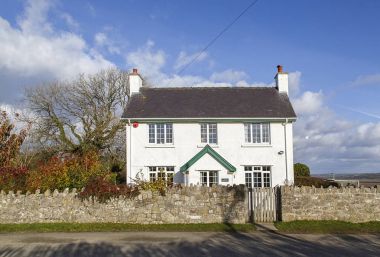 Gower, Wales, UK: November 10, 2016: A white detached cottage set in a rural country lane on the Gower peninsular with a front stoop and surrounding stone wall a with garden gate. clipart
