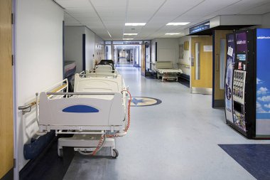 Hastanede boş bir koridor. Koridor temiz. Yedek hastane sedyeleri ve içme suyu satan bir otomat var.. 