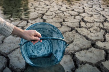 Kadın elleri çatlamış zeminde su topluyor, su kıtlığı var.