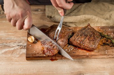 Erkek el Close-Up ızgara et baharatlar ile ahşap tahta üzerinde kesmek.