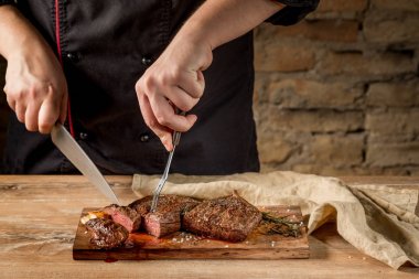 Erkek el Close-Up ızgara et baharatlar ile ahşap tahta üzerinde kesmek.