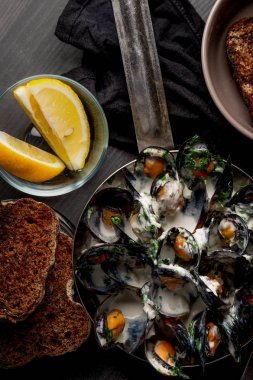 Midye tava, ekmek ve limon dilimleri kase Dor mavi soslu üstten görünüm siyah masada