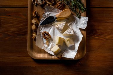 Brie peyniri dilimleri, otlar, fındık ve ahşap tepsi, bıçakta kopya alanı görünümüyle top