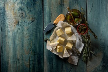 kopya alanı ile mavi ahşap arka plan üzerinde brie peyniri, bıçak, otlar ve kavanoz zeytin ve capperi ile Üstten Görünüm