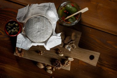 brie peyniri, bıçak, otlar ve kavanoz zeytin ve capperi rustik ahşap masa üzerinde düz lay
