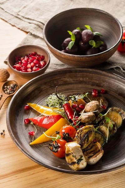 grilled and stuffed vegetables, plums and pomegranate grains on wooden table, close up