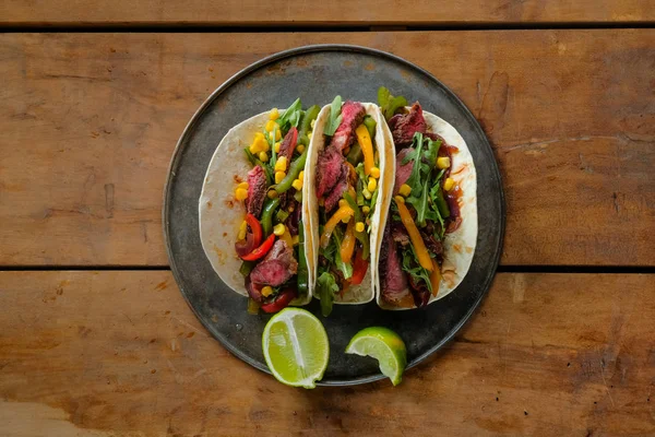 Deliziosi Tacos Con Fette Lime Piastra Nera Sfondo Legno Vista — Foto Stock