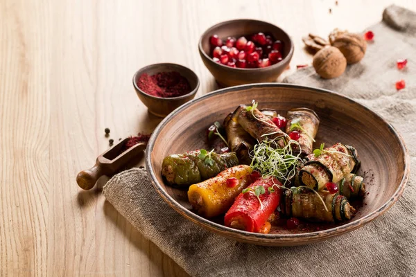 top view of grilled and stuffed vegetables on plate and pomegranate grains in bowl on wooden table with copy space