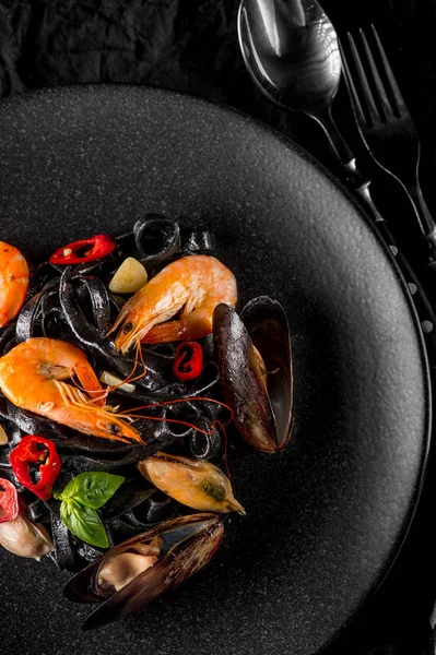 oysters, shrimps and peppers on black plate with spoon and fork, top view