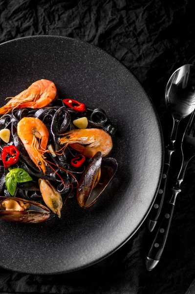 oysters, shrimps and peppers on black plate with spoon and fork, top view