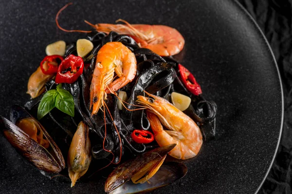 oysters, shrimps and peppers on black plate, top view