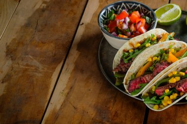 spicy tacos with lime slices and cut vegetables in bowls on wooden table, top view with copy space clipart