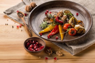 Nar ile kase tahıllar, ahşap masa üzerinde baharatlar ile plaka, ceviz ve tahta kaşık ızgara sebze, yakın çekim