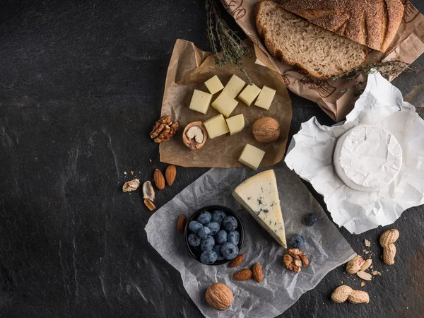 Assorted Cheese Slices Wooden Board Olive Oil Blueberries Nuts Stone — Stock Photo, Image