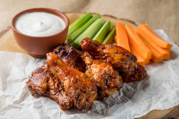 Buffalo chicken wings on wooden board served with cheese sauce and celery and carrot sticks. top view