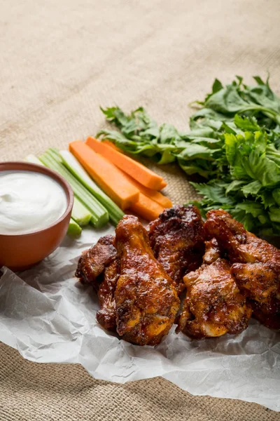 Buffalo chicken wings with celery and carrot sticks served with cheese sauce on rustic cloth