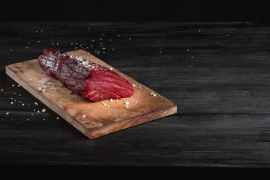 Siyah arka plan üzerine kaba deniz tuzu ile doğrama tahtası üzerinde ham taze sığır filetosu