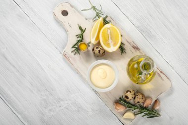 Bıldırcın yumurta, zeytinyağı, limon, diş sarımsak ve biberiye Beyaz ahşap kesme tahtası, kopya alanı ile üstten görünüm üzerinde sos