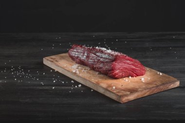 Siyah arka plan üzerine kaba deniz tuzu ile doğrama tahtası üzerinde ham taze sığır filetosu