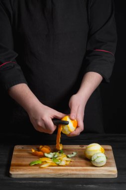 Şef eller turuncu bıçakla ahşap tahta üzerinde peeling..