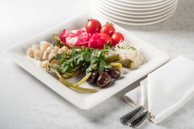 Turşu ile yeşillik, domates, kırmızı biber, salatalık, zeytin ve sarımsak ile mutfak eşyaları, beyaz tabakta servis yakın çekim