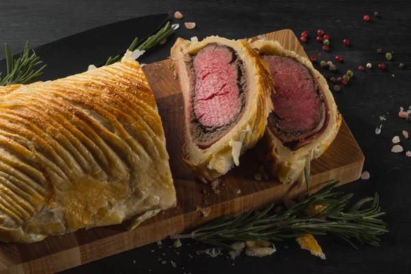 sliced beef wellington on wooden board with spices, close up