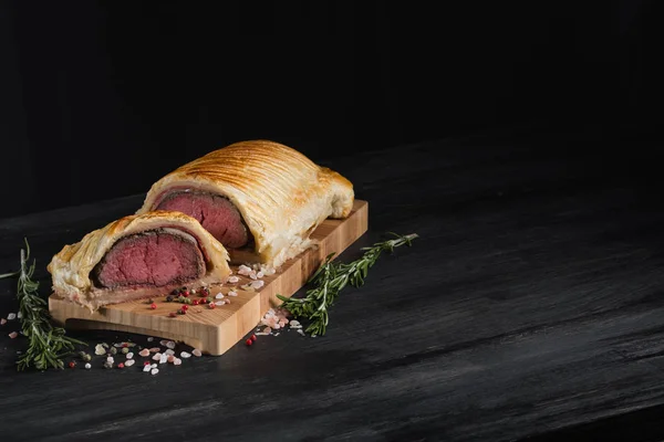 Beef wellington with rosemary and spices on wooden board