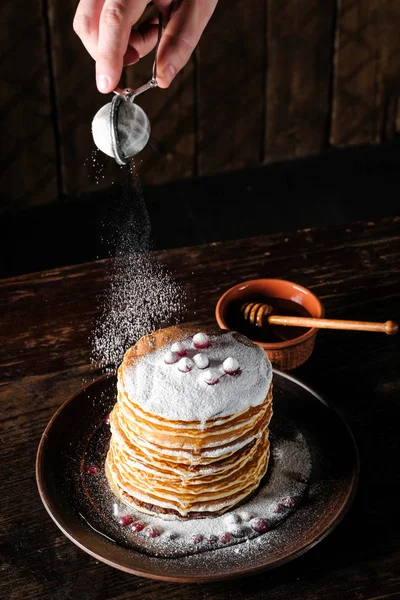 chef hand putting white sugar powder on pancakes over dark wooden background with copy space
