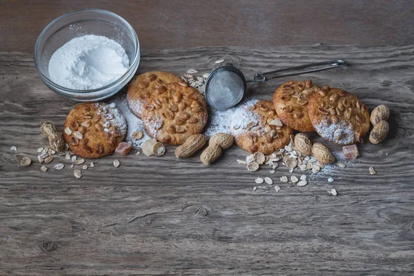 Chocolate cookies with sugar powder in bowl and utensils on wooden background with copy space