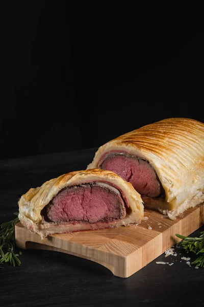 close up of beef wellington on wooden board with herbs and spices