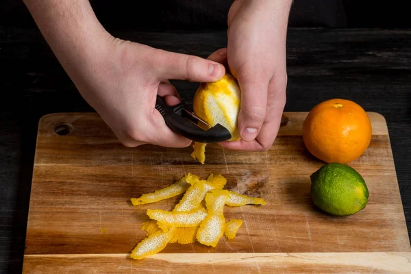 chef hands peeling lemon with knife over wooden board, close up